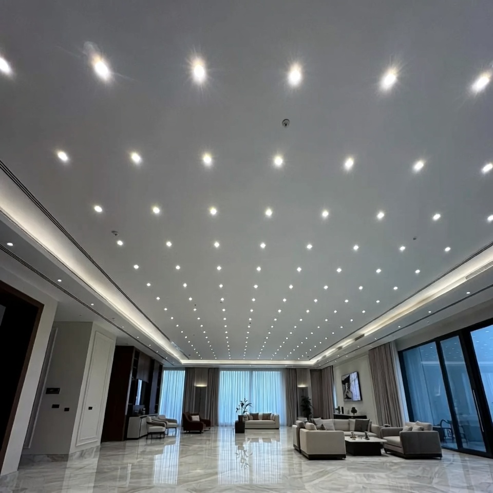 Luxury villa living room with excessive recessed downlights covering the ceiling, dozens of bright LED downlights arranged everywhere, ceiling full of light spots like a grid, overly bright and flat illumination, no shadows, no visual depth, architectural details washed out, marble floor and luxury furniture appearing lifeless, uncomfortable glare, sterile atmosphere similar to a showroom or hospital lobby, poor lighting design, no layered lighting, no focal point, cold white lighting, high-end interior ruined by excessive downlights, realistic architectural photography, ultra realistic, 8k, editorial interior design magazine style, no people, 16:9