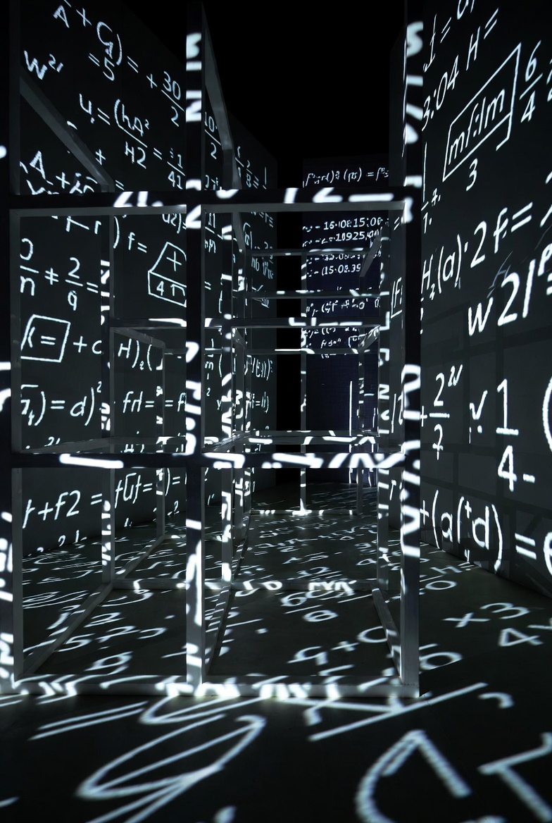 A photograph of an abstract environment with mathematical equations and geometric shapes, illuminated by artificial lighting, emphasizing physics and engineering.