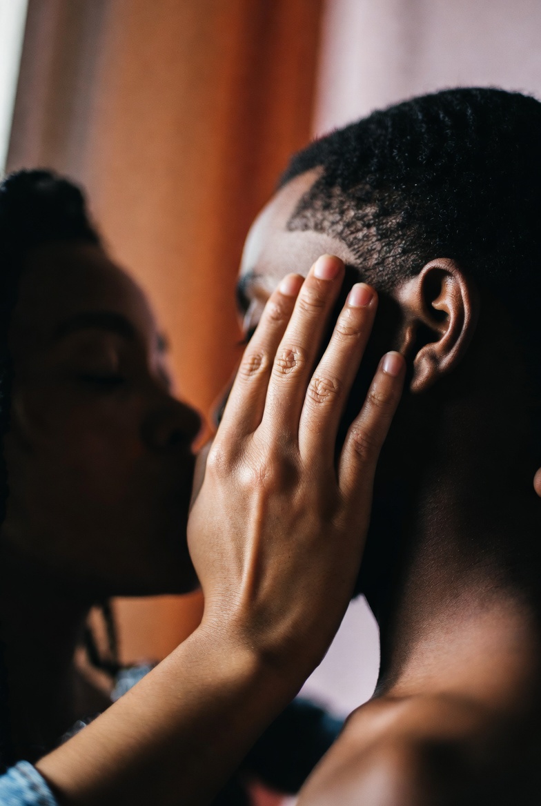 A photograph of an intimate moment with a hand touching a cheek in a warm, softly lit setting.