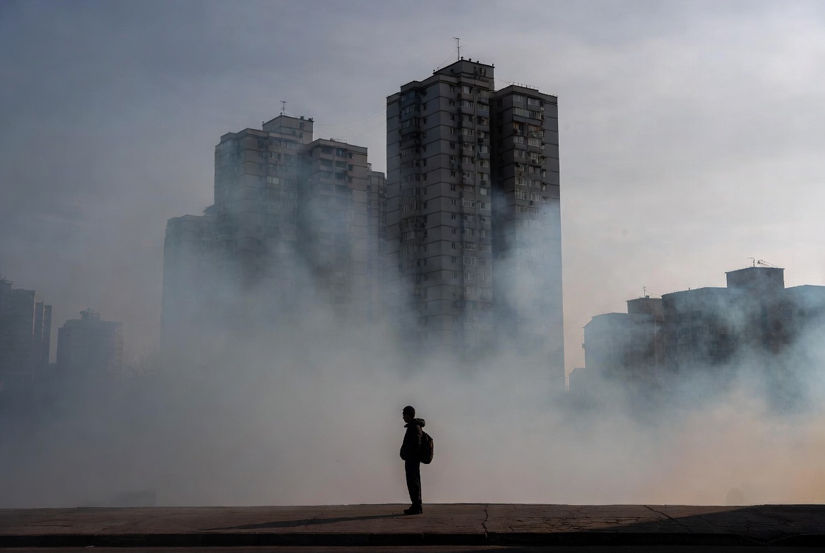 A photograph of a smoggy cityscape with a solitary figure, illustrating rising urban living costs.